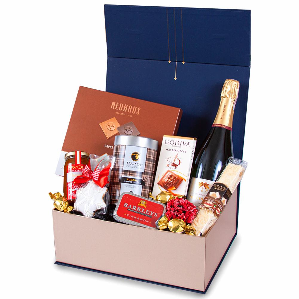Elegancki, otwarty granatowy kosz prezentowy z różowym wnętrzem, wypełniony luksusowymi słodyczami, czekoladkami Godiva i Neuhaus, ciasteczkiem w kształcie gwiazdy z czerwoną kokardką, konfiturą...