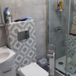 Nowoczesna łazienka z kabiną prysznicową, wiszącą toaletą, umywalką z szafką i szarymi płytkami z wzorem gwiazd na zabudowie stelaża.