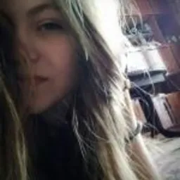 Portret młodej kobiety z długimi blond włosami, leżącej na wzorzystym dywanie, z głową opartą na ręce, w nieostrym tle widać fragment drewnianego mebla.