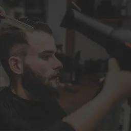 Fryzjer stylizuje brodatemu mężczyźnie włosy grzebieniem, przygotowując je do suszenia suszarką.