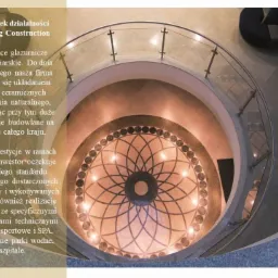 Wewnętrzna klatka schodowa z dekoracyjną posadzką z kamienia naturalnego ułożoną we wzór rozety, widok z góry, szklane balustrady