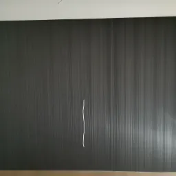 Ciemna ściana z tapetą w pionowe prążki. Widoczny kabel zwisający ze ściany i gniazdka elektryczne w dolnym rogu.