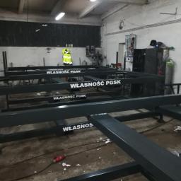 Badura Welding - Konstrukcja metalowa z napisem 'WŁASNOŚĆ PGSK' na hali produkcyjnej, widoczny pracownik w kamizelce odblaskowej w tle.