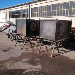Badura Welding - Dwa surowe, metalowe zbiorniki na spawanych konstrukcjach wsporczych, stojące na zewnątrz hali z rzędem okien, widoczne ślady spawania i obróbki metalu.