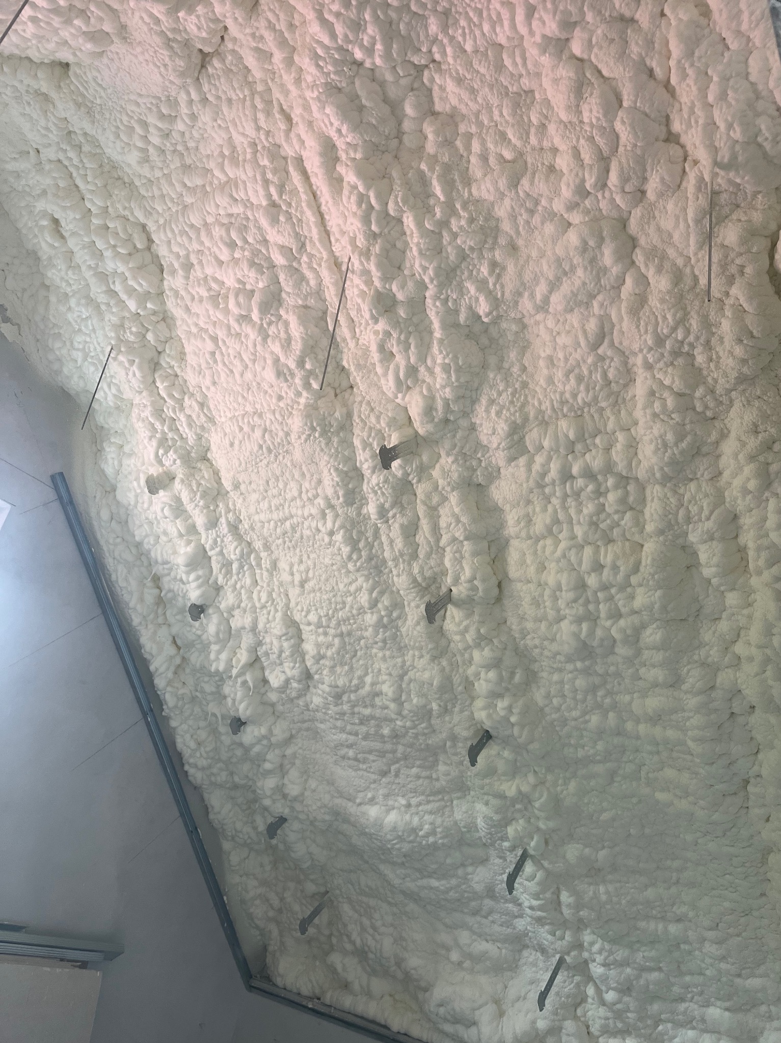 Ocieplenie poddasza pianką PUR z widocznymi mocowaniami, wykonane natryskowo, tworzące jednolitą warstwę izolacyjną o nieregularnej fakturze.