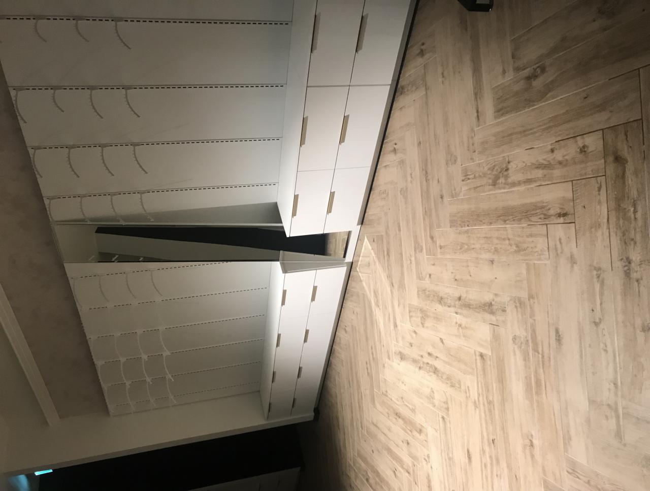 Wnętrze garderoby z białymi szafami i parkietem ułożonym w jodełkę, widziane z perspektywy podłogi.