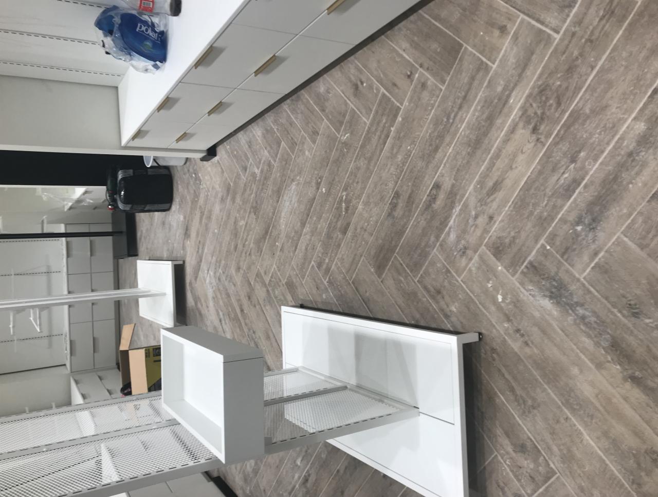 Podłoga z płytek ułożonych w jodełkę w nowym biurze z białymi meblami i jeszcze nieuprzątniętymi śladami po remoncie w postaci drobnych zabrudzeń na podłodze.