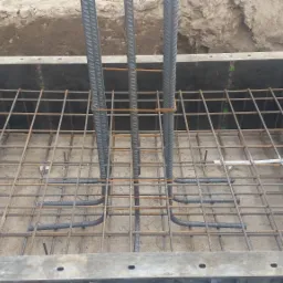 Zbrojenie fundamentu w szalunku z widocznymi pionowymi prętami i siatką zbrojeniową. Detal budowy, betonowa podstawa z elementami stalowymi.