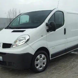 Biały samochód dostawczy Renault Trafic na mokrym placu, z widocznym logo 'Optimum' na przednim zderzaku.