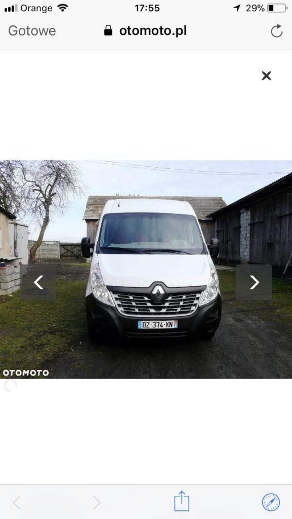 Biały samochód dostawczy Renault Master zaparkowany na trawiastym terenie przed drewnianym budynkiem gospodarczym