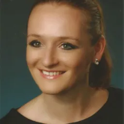 Portret uśmiechniętej kobiety z kolczykiem w kształcie nuty na tle ciemnego, lekko niebieskiego tła.