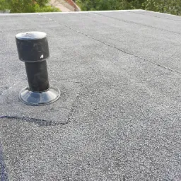 Płaski dach pokryty papą z widocznym kominkiem wentylacyjnym, uszczelnionym bitumiczną masą.