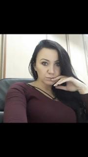 Portret kobiety w bordowej bluzce, siedzącej w biurze, z dłonią pod brodą, sugerujący zamyślenie lub oczekiwanie na klienta.