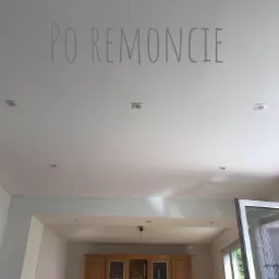 Jasny sufit z wpuszczonymi punktami świetlnymi i napisem 'PO REMONCIE', widok na drewnianą zabudowę meblową w głębi pomieszczenia.