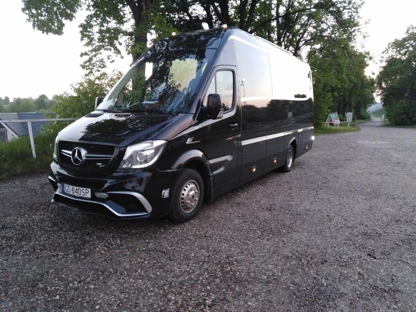 Czarny, luksusowy bus Mercedes-Benz Sprinter z przyciemnianymi szybami, zaparkowany na żwirowym podłożu w Gdańsku, z widocznymi drzewami w tle.
