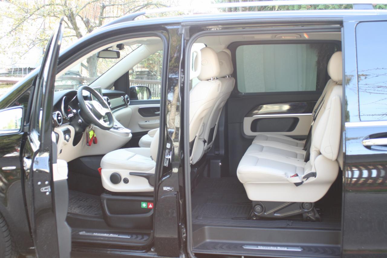 Wnętrze czarnego vana Mercedes-Benz z beżową skórzaną tapicerką, otwarte drzwi przesuwne i przednie, widoczne fotele pasażerów i kierowcy.