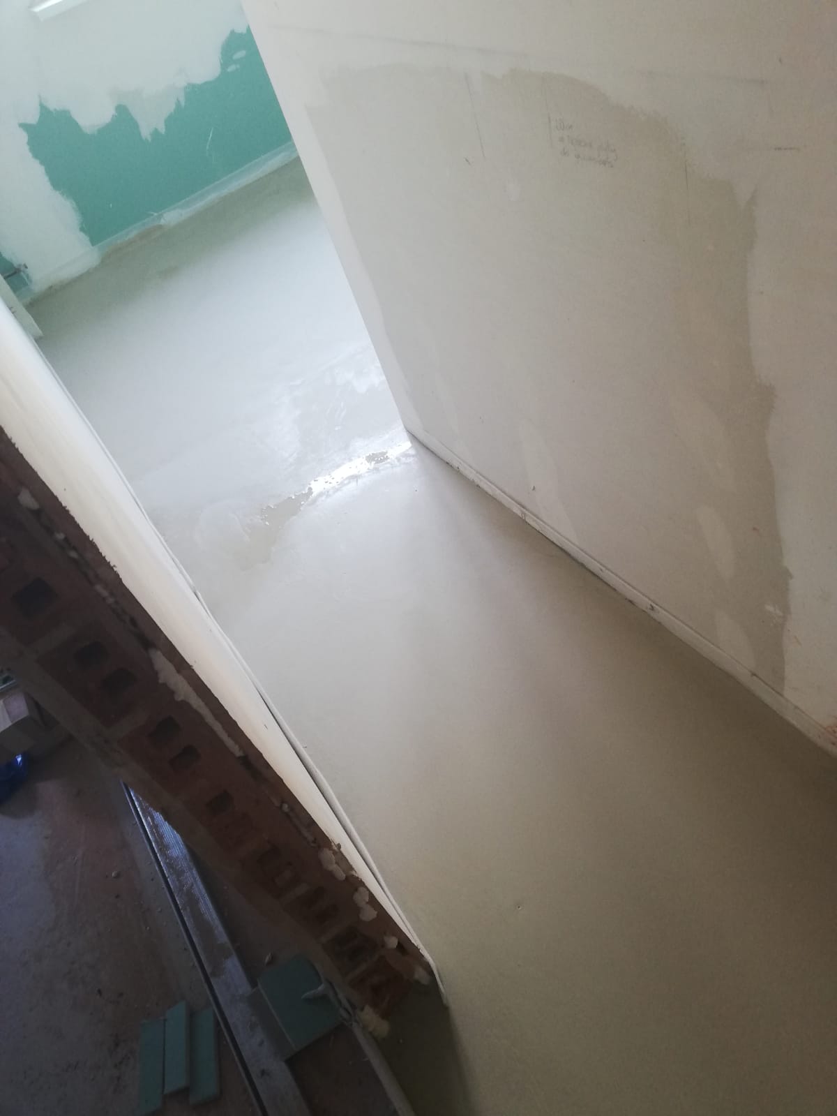 Świeżo wylana, samopoziomująca wylewka podłogowa w trakcie schnięcia, widoczne ślady po narzędziach i niewielkie nierówności, ściany przygotowane do malowania, surowy stan wnętrza.