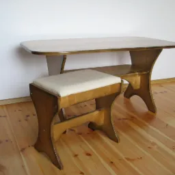 Drewniany stolik z zaokrąglonymi krawędziami i półką pod blatem, w komplecie z tapicerowanym stołkiem na giętych nogach, ustawione na parkiecie w pomieszczeniu z białymi ścianami.