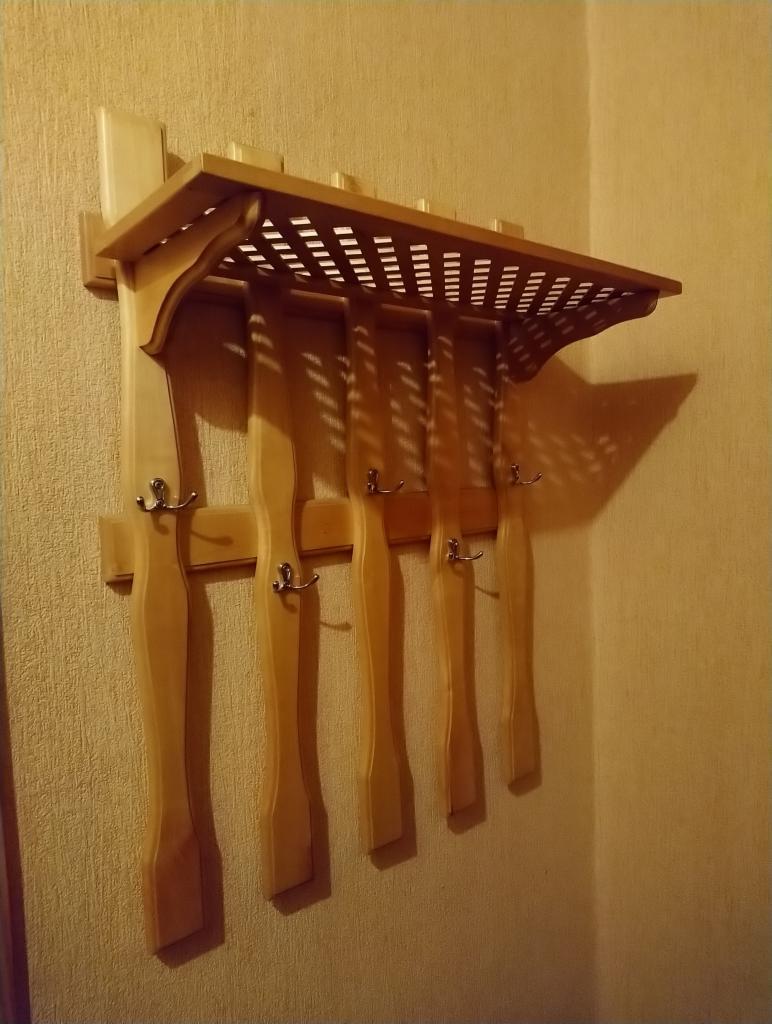 Drewniany wieszak ścienny z półką i pięcioma haczykami, wykonany z jasnego drewna, zamontowany na beżowej ścianie.