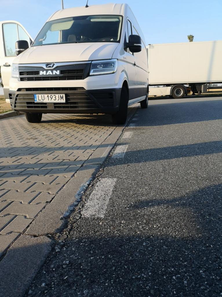 Biały bus MAN z otwartymi drzwiami i numerem rejestracyjnym LU 193JM stoi obok naczepy na parkingu w słoneczny dzień. Widok z dołu.