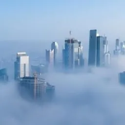 Panorama Dubaju spowita poranną mgłą, widoczne drapacze chmur w trakcie budowy, żurawie budowlane wystające ponad chmury.