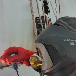 Spawacz w kasku 3M, zabezpieczony linami alpinistycznymi, spawa metalową konstrukcję na wysokości, widoczna spawarka inwertorowa.