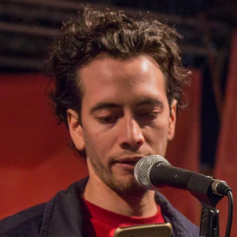 Młody mężczyzna z mikrofonem, prawdopodobnie lektor lub nauczyciel języków obcych, prowadzący zajęcia online. Widoczny smartfon.