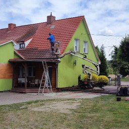 STAEM Michał Kaźmierski - Pracownik na podnośniku koszowym czyści czerwoną dachówkę domu o jaskrawozielonej elewacji, widoczna różnica między umytą a brudną częścią dachu.