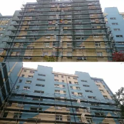 Wielopiętrowy budynek mieszkalny w trakcie renowacji elewacji, z widocznymi rusztowaniami i fragmentami pomalowanej na niebiesko oraz pozostawionej w oryginalnym, jasnym kolorze części fasady.