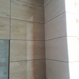 Beżowe płytki imitujące trawertyn na ścianie, z dekoracyjnym pasem płytek z geometrycznym wzorem u dołu, widok z narożnika.