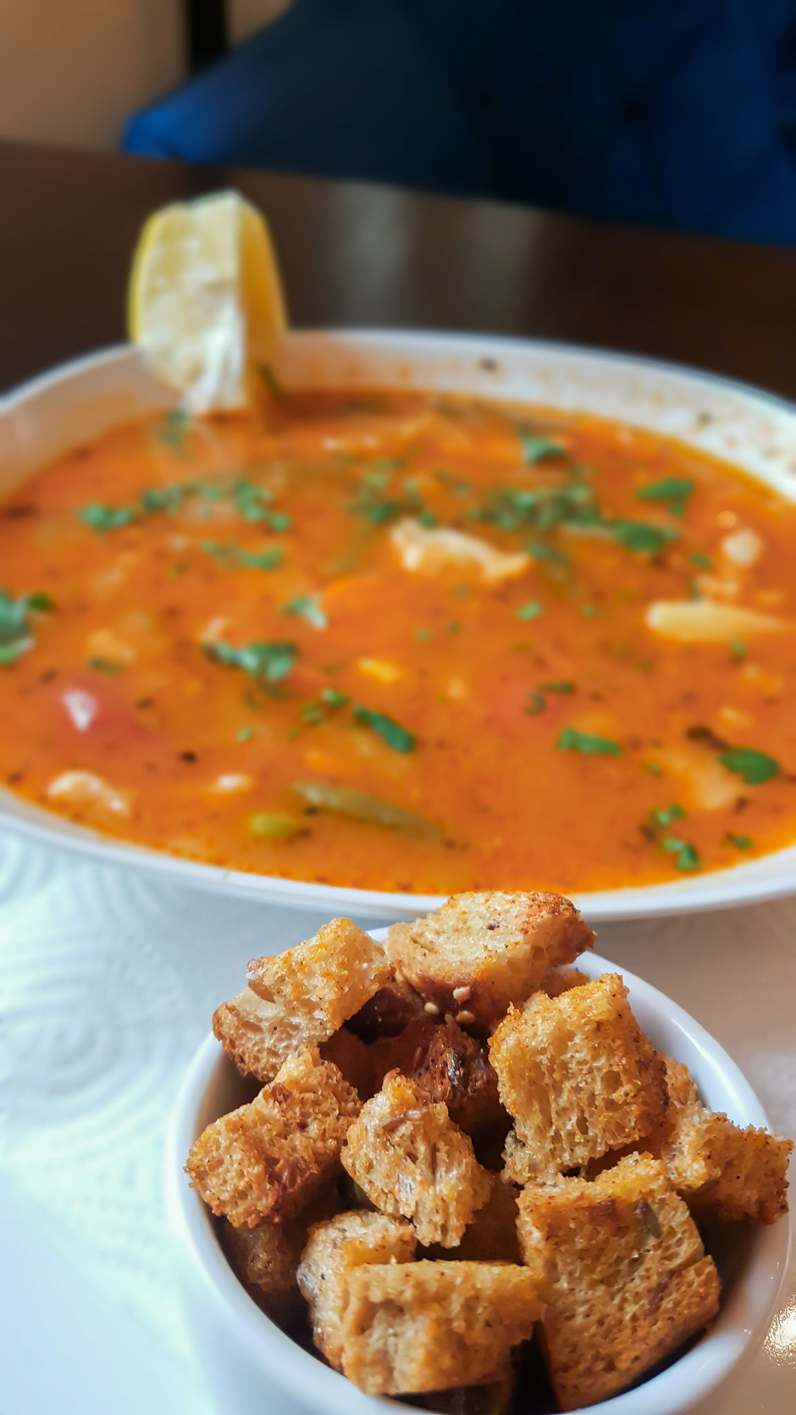 Aromatyczna zupa pomidorowa z ziołami i cytryną w białym talerzu, podana z grzankami w małej miseczce.