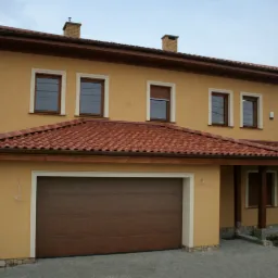 Ocieplona elewacja dwukondygnacyjnego domu z brązową bramą garażową, czerwoną dachówką i oknami w brązowych ramach.