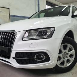 F.H.U. Painting Teddy Bear Dawid Kostkowski - Białe Audi Q5 po naprawie blacharsko-lakierniczej, widoczne z przodu, z lekkim kątem, na tle warsztatu.