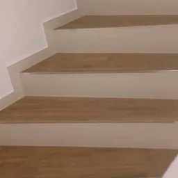 Wykończone schody z drewnopodobnymi panelami na stopniach i jasnymi płytkami na podstopnicach oraz krawędziach, widok z dołu.