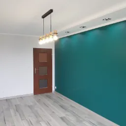 Pomalowane na szmaragdowo ściany w pustym pokoju z drewnianą podłogą i nowoczesną lampą sufitową