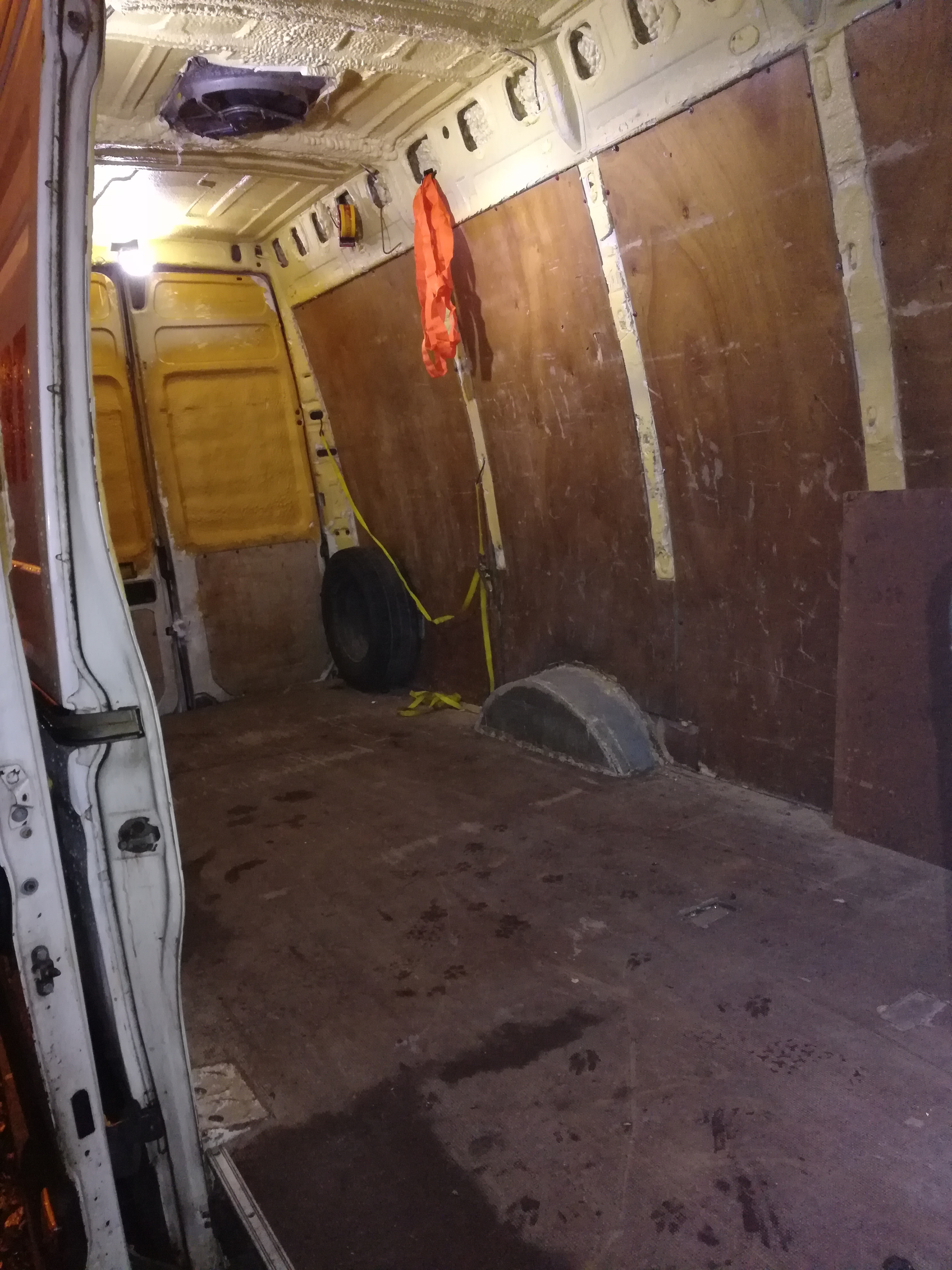 Wnętrze częściowo wykończonego busa z zamontowanym wentylatorem dachowym, zabezpieczonym kołem zapasowym i pomarańczową kamizelką odblaskową.