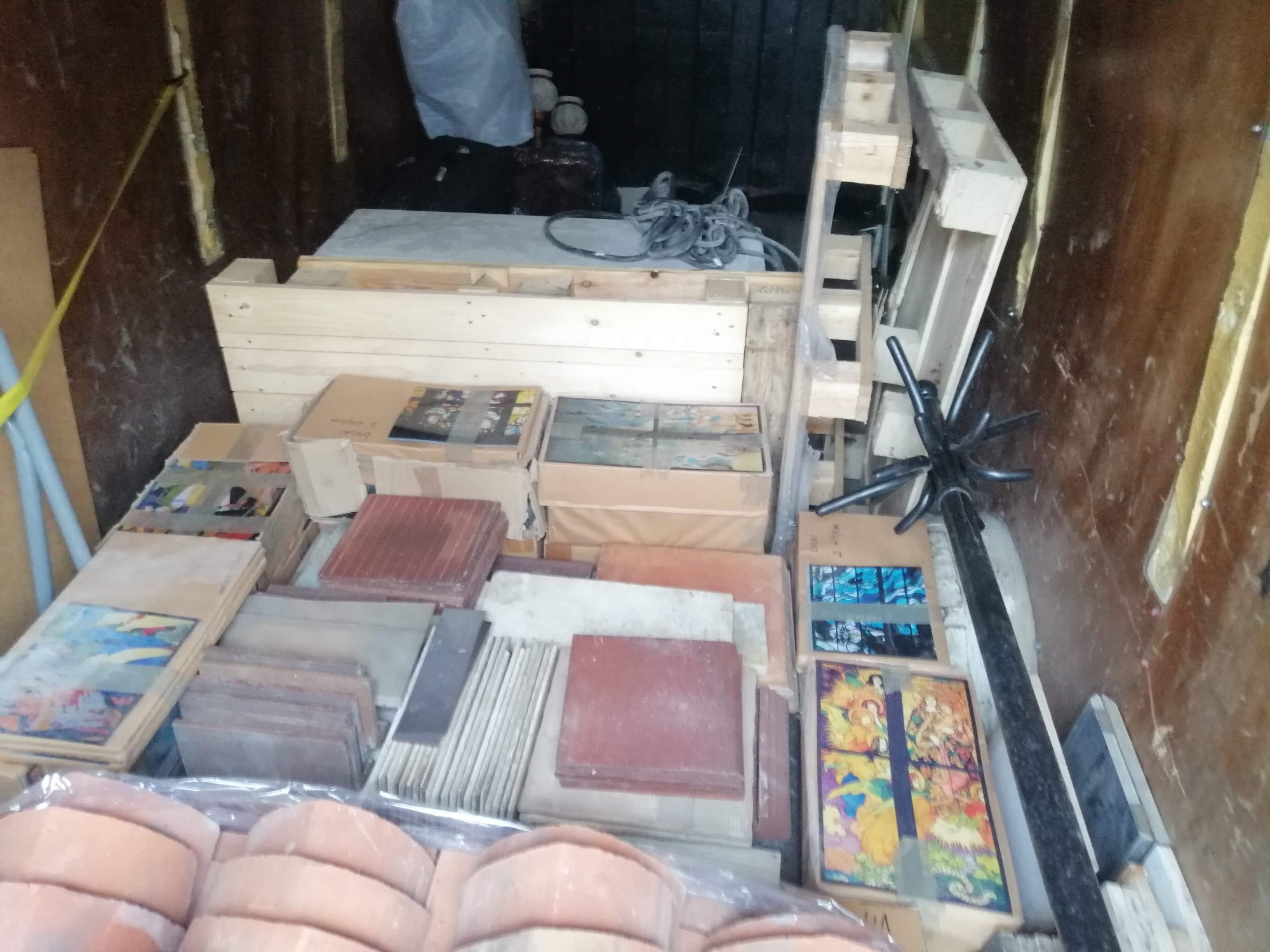 Wnętrze przestrzeni ładunkowej z paletami, pudełkami, dachówkami i płytkami ceramicznymi przygotowanymi do transportu.