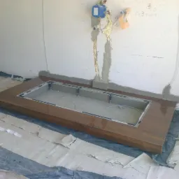 Przygotowanie do montażu brodzika z obudową z płytek imitujących drewno, widoczne instalacje wodne na ścianie, zabezpieczona podłoga i ściany w trakcie prac.
