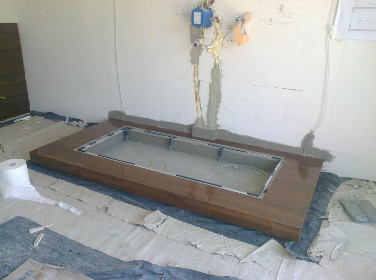 Przygotowanie do montażu brodzika z obudową z płytek imitujących drewno, widoczne instalacje wodne na ścianie, zabezpieczona podłoga i ściany w trakcie prac.