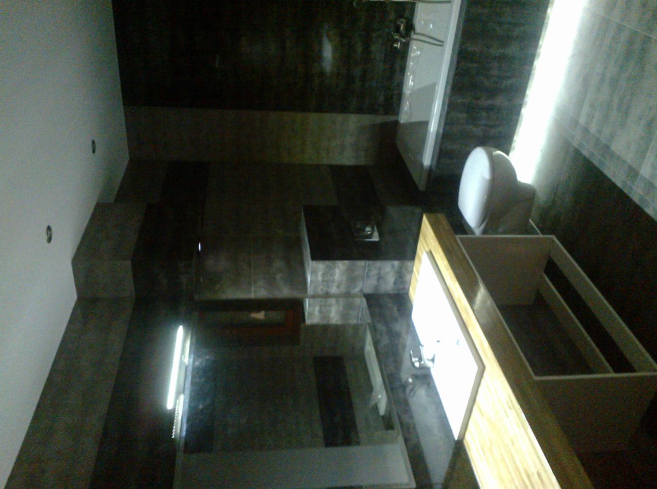 Nowoczesna łazienka z ciemnymi płytkami, białą armaturą i drewnianą szafką pod umywalką, widok z góry.