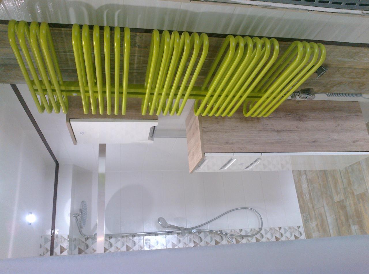 Nowoczesna łazienka z zielonym grzejnikiem drabinkowym, drewnopodobną szafką wiszącą z białymi frontami i kabiną prysznicową z biało-beżową mozaiką.