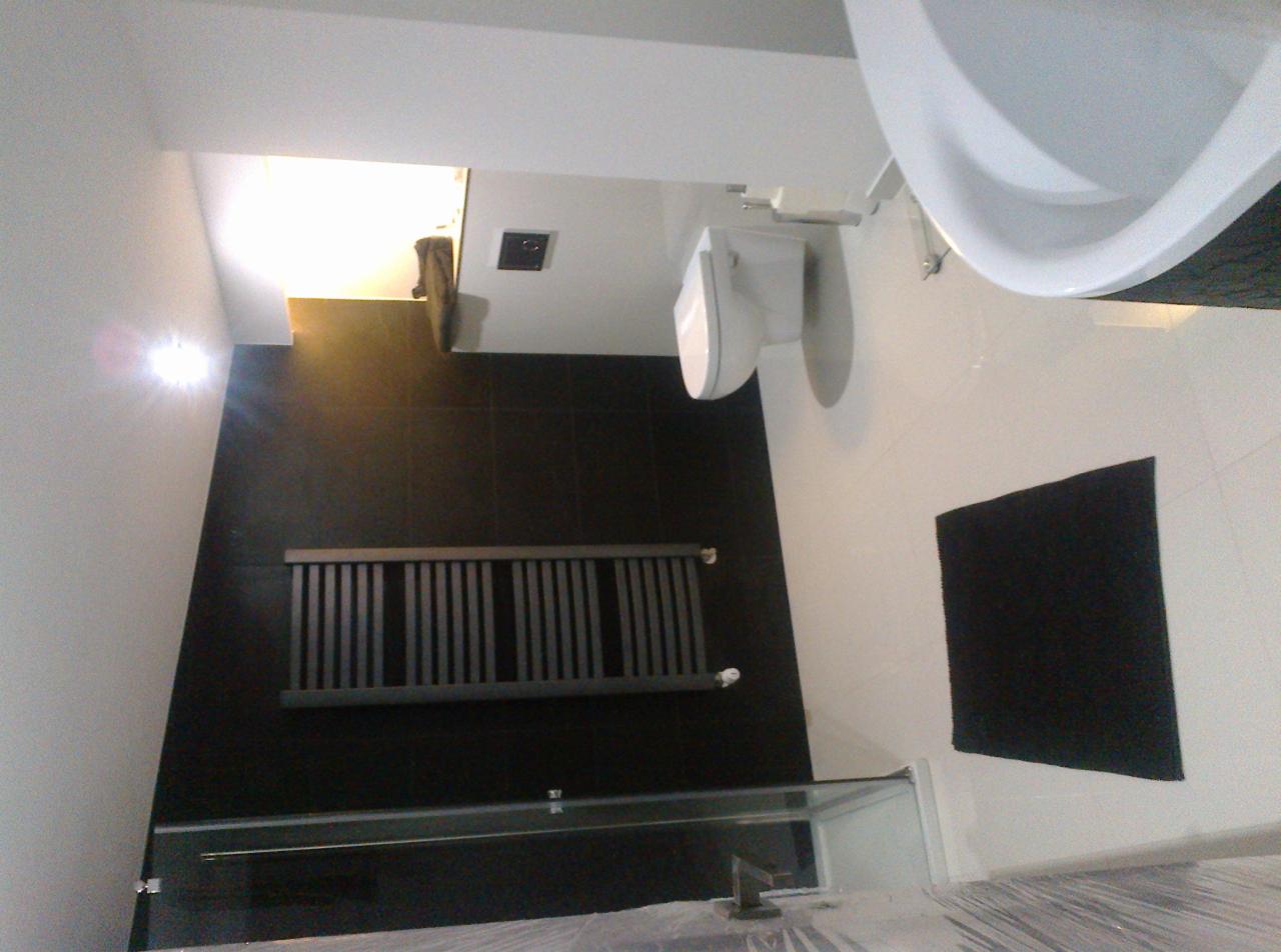 Nowoczesna łazienka z czarnymi płytkami, grzejnikiem drabinkowym i białą armaturą, widok z góry.