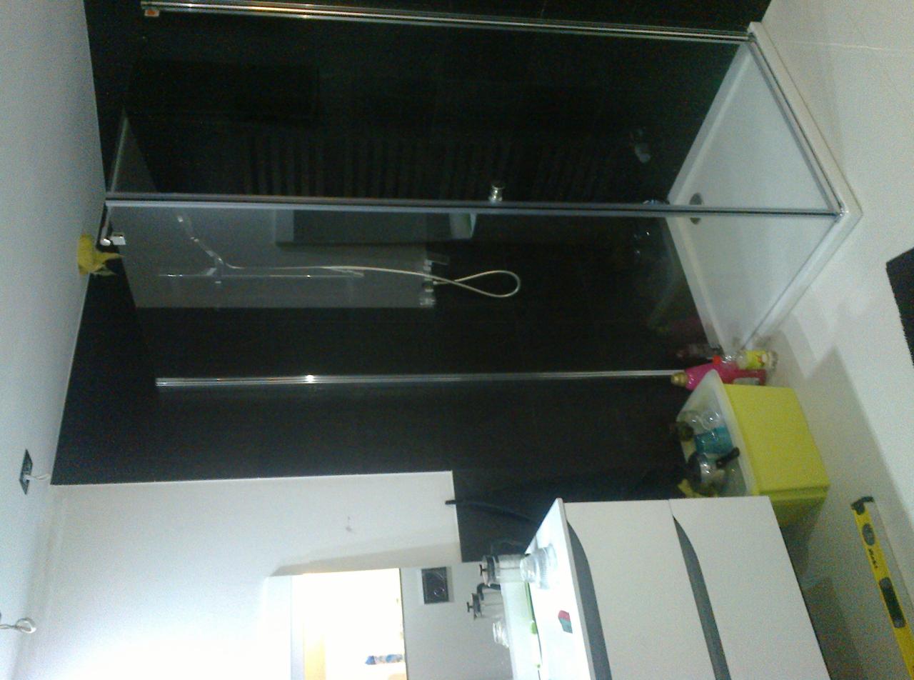 Szklana kabina prysznicowa z brodzikiem, zamontowana w łazience z czarnymi płytkami, widoczna skrzynka z narzędziami i poziomica.