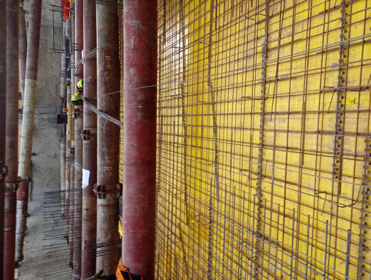 Żółte szalunki z siatką zbrojeniową i podpory pionowe z rur, widoczny pracownik w odblaskowej kamizelce na wysokości.