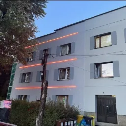 Budynek mieszkalny w Przemyślu po remoncie elewacji, z szarymi ścianami i okiennicami, widoczne poziome linie wyznaczające obszary prac na wysokościach, drabina oparta o ścianę.