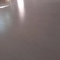 Jasne panele podłogowe ułożone wzdłużnie, z widocznym połyskiem i refleksami światła słonecznego wpadającego do pomieszczenia.