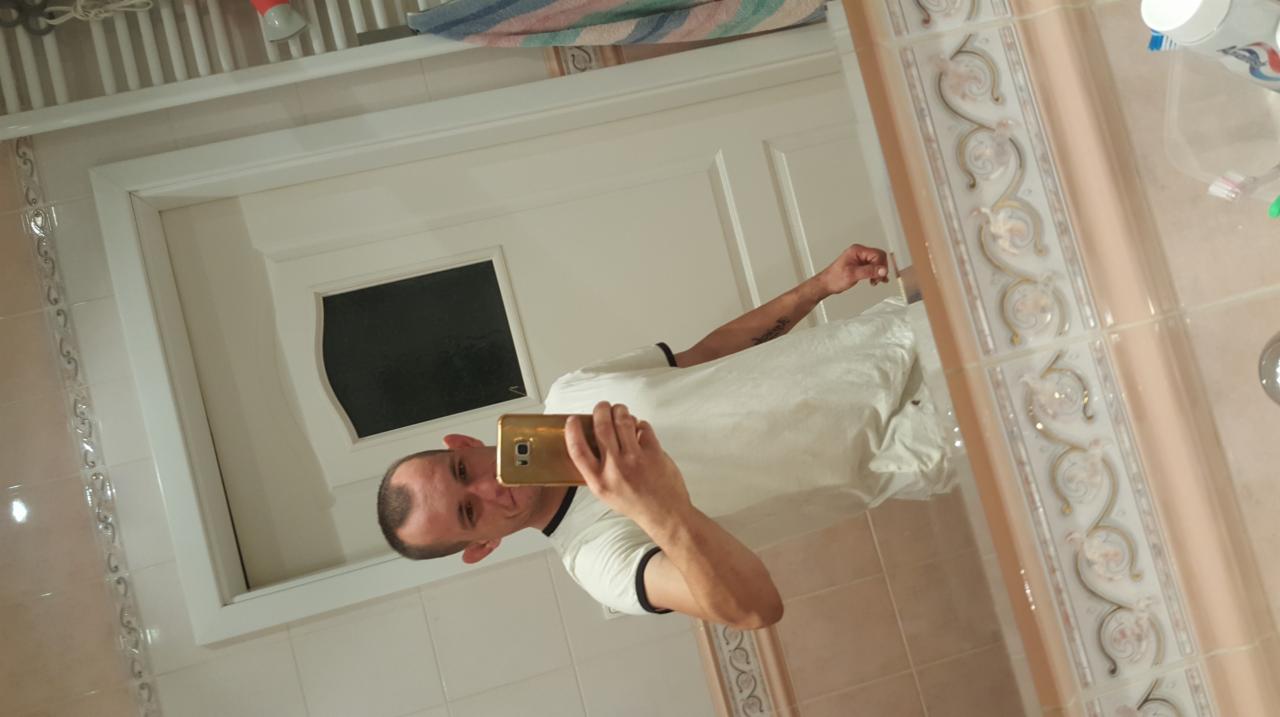 Mężczyzna robi selfie w łazience po remoncie. Widoczne płytki z dekoracyjnym wzorem i białe drzwi z czarną szybą. Odnowione wnętrze.