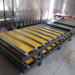 Dwu-poziomowy, modułowy system przenośnik&oacute;w rolkowych z ż&oacute;łtymi panelami i stalowymi rolkami, widoczne mechanizmy łańcuchowe, w tle metalowa ściana hali i kartony.