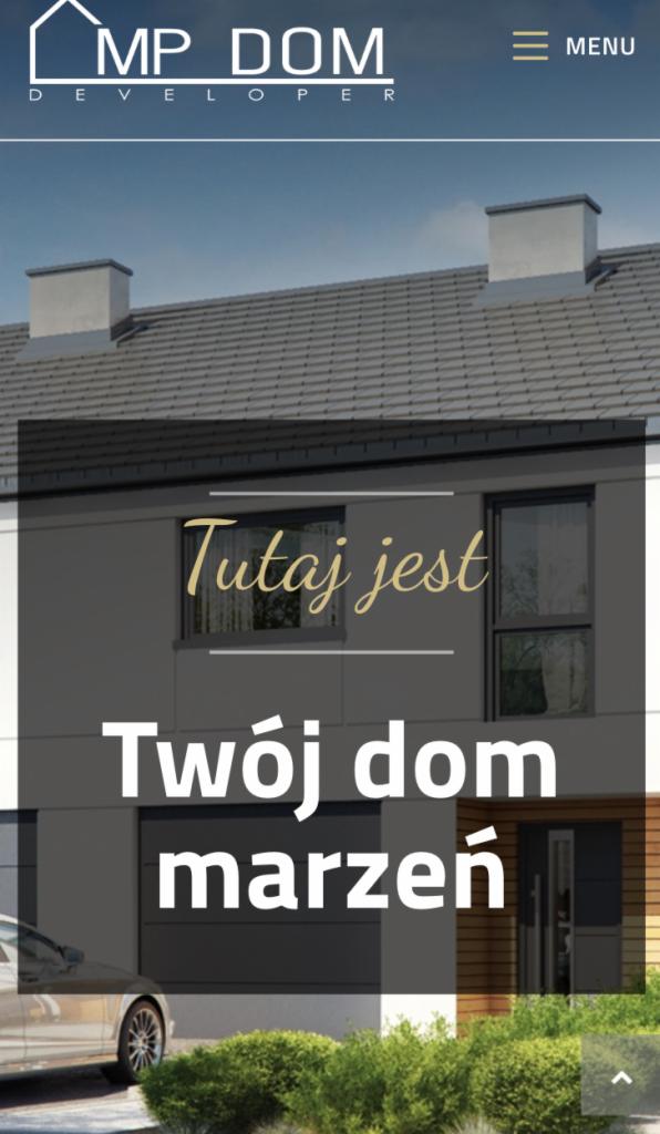 Wizualizacja domu jednorodzinnego z szarą elewacją, garażem i napisem 'Tutaj jest Twój dom marzeń', widoczny fragment samochodu i zieleni.