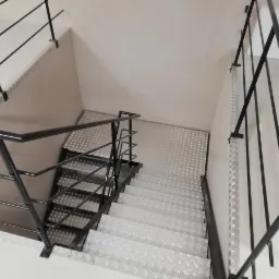 Klatka schodowa z metalowymi schodami i czarną, metalową balustradą z poręczą, widok z góry.